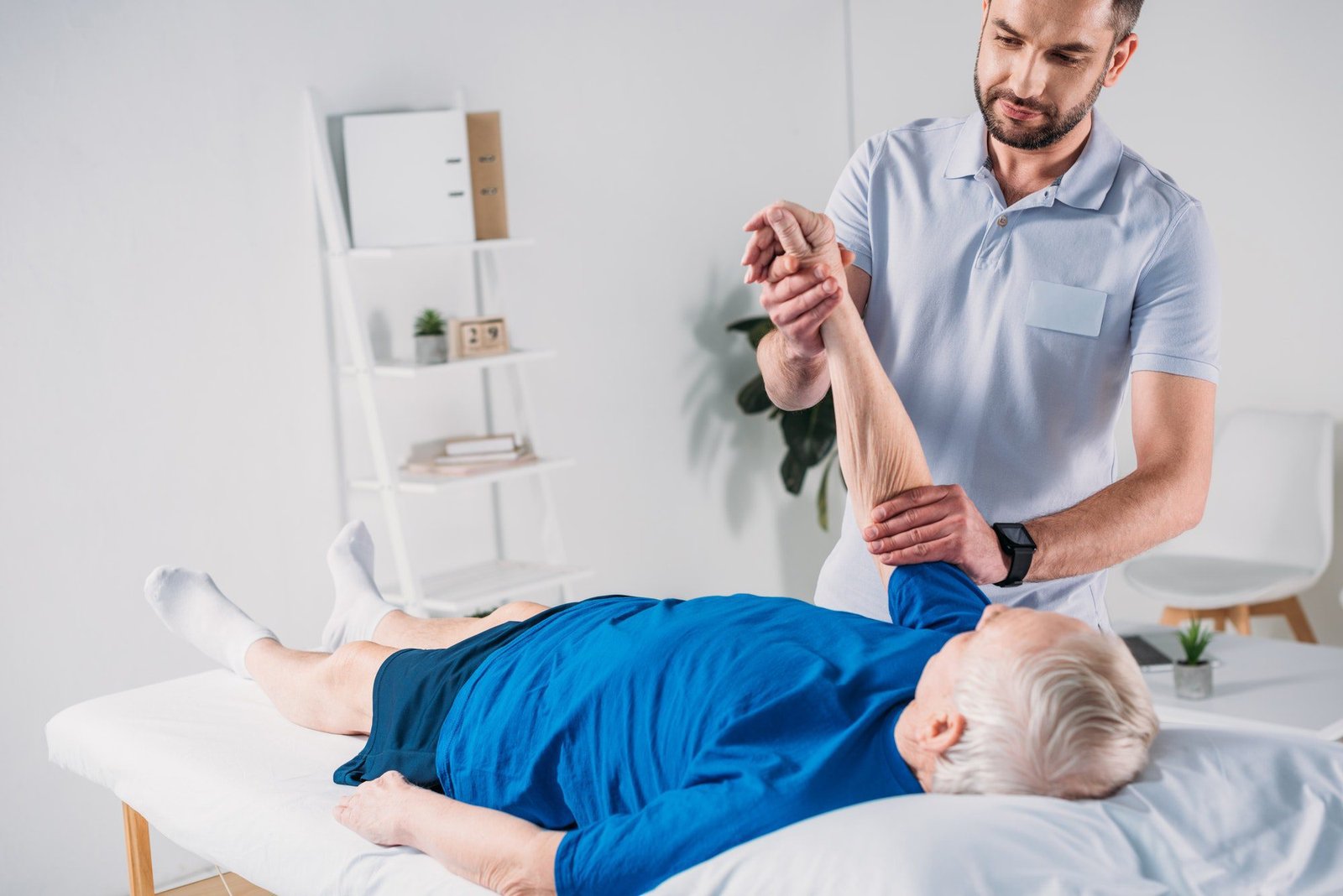 focused physiotherapist doing massage to senior man on massage table