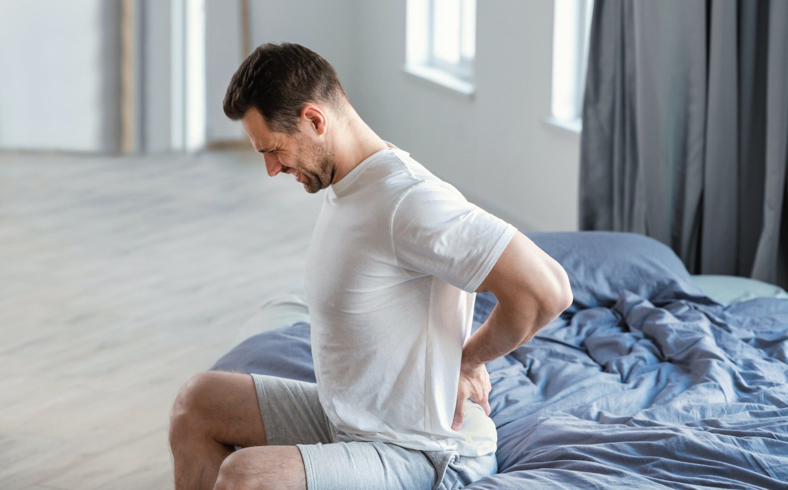 Man Massaging Aching Back Sitting In Bed At Home