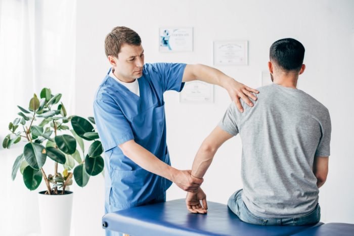 Physiotherapist massaging arm of patient on massage table in hospital