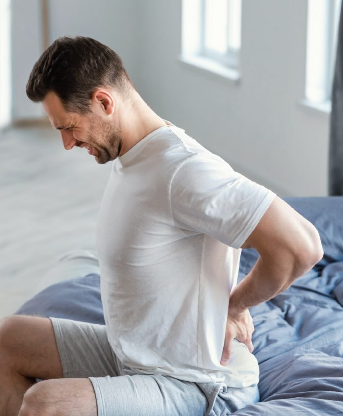 Man Massaging Aching Back Sitting In Bed At Home Man Massaging Aching Back Sitting In Bed At Home